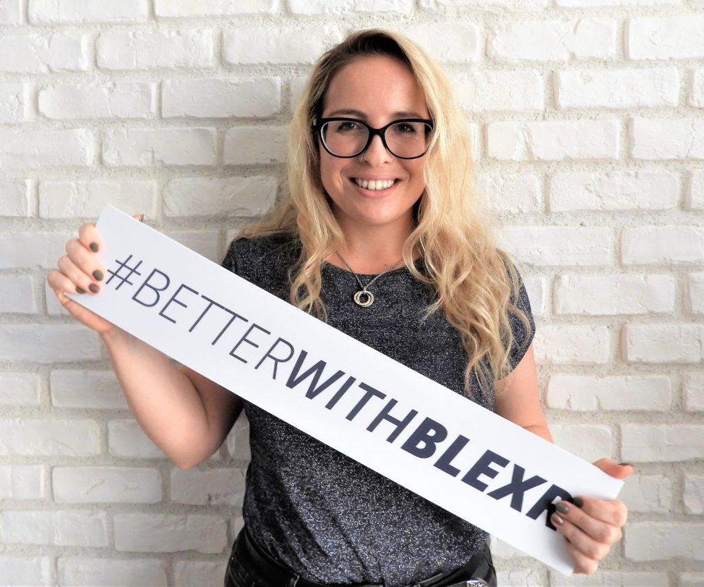 A woman holding a sign that says "#BetterWithBlexr"